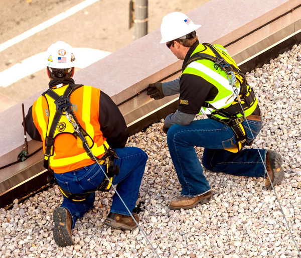 photo of two construction workers wearing fall protection gear near the edge of a roof